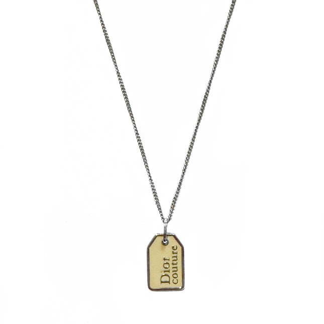 Christian Dior silver necklace with tag shape that says Dior couture in silver inside cream enamel inlay.